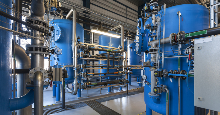 Industrial facility interior with large blue tanks and complex piping system.