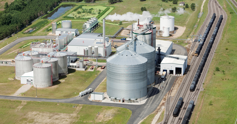 Aerial view of an industrial ethanol production plant with storage tanks and train tracks.