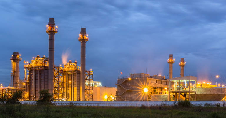 Industrial power plant at dusk with glowing lights and tall chimneys.