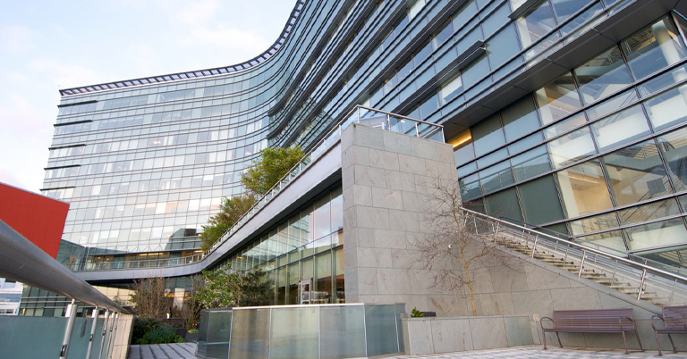 Modern glass office building with greenery and outdoor benches.