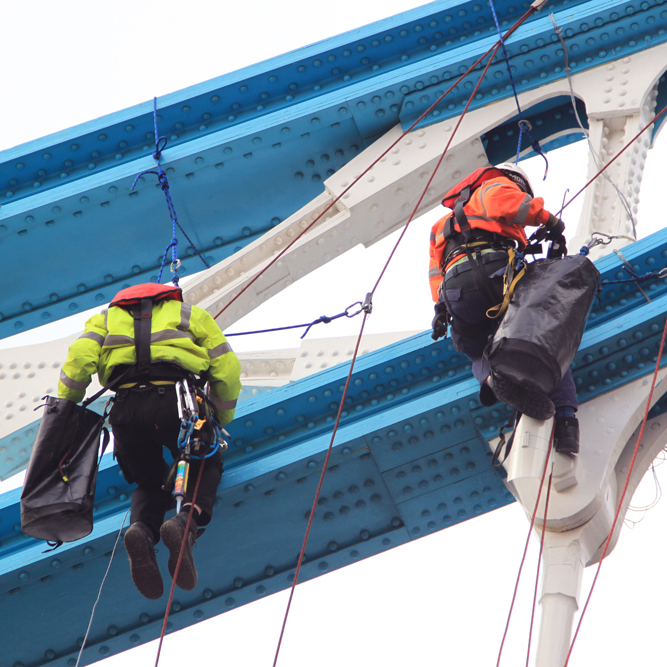Workers in bright jackets hanging on ropes for bridge maintenance.