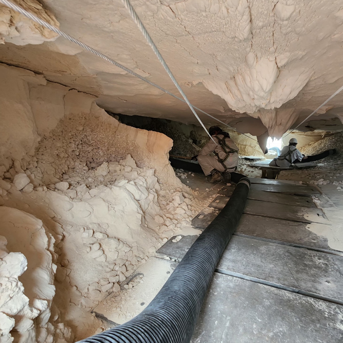Two people working in a narrow cave with support ropes and ventilation hose.
