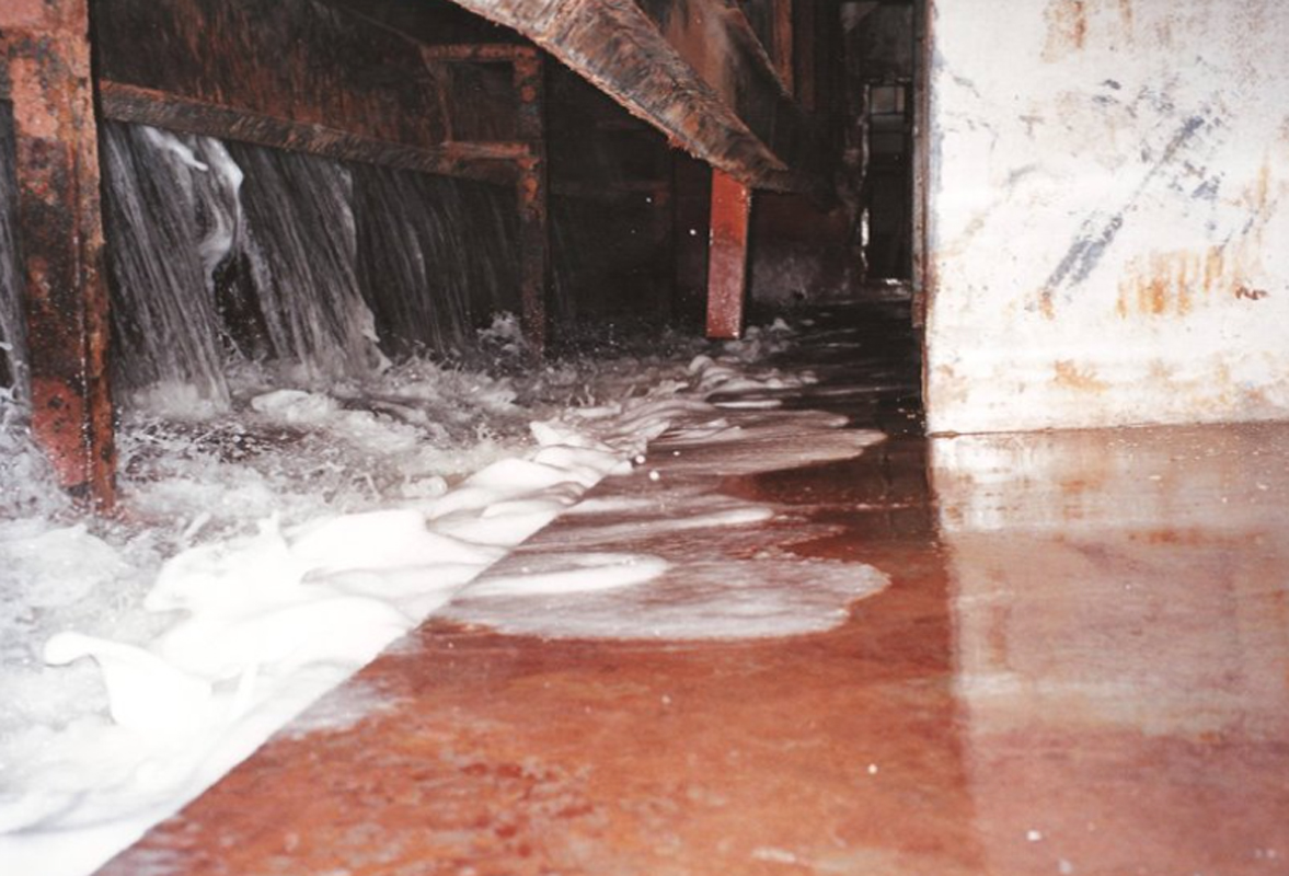 Water flowing from industrial machinery onto a rusted floor.