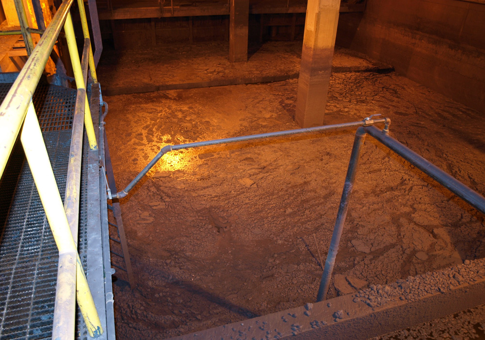 Industrial sediment basin with metal railings and textured floor, illuminated by warm lighting.