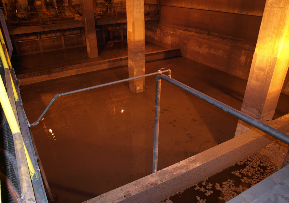 Industrial water treatment tank with metal railings under dim lighting.